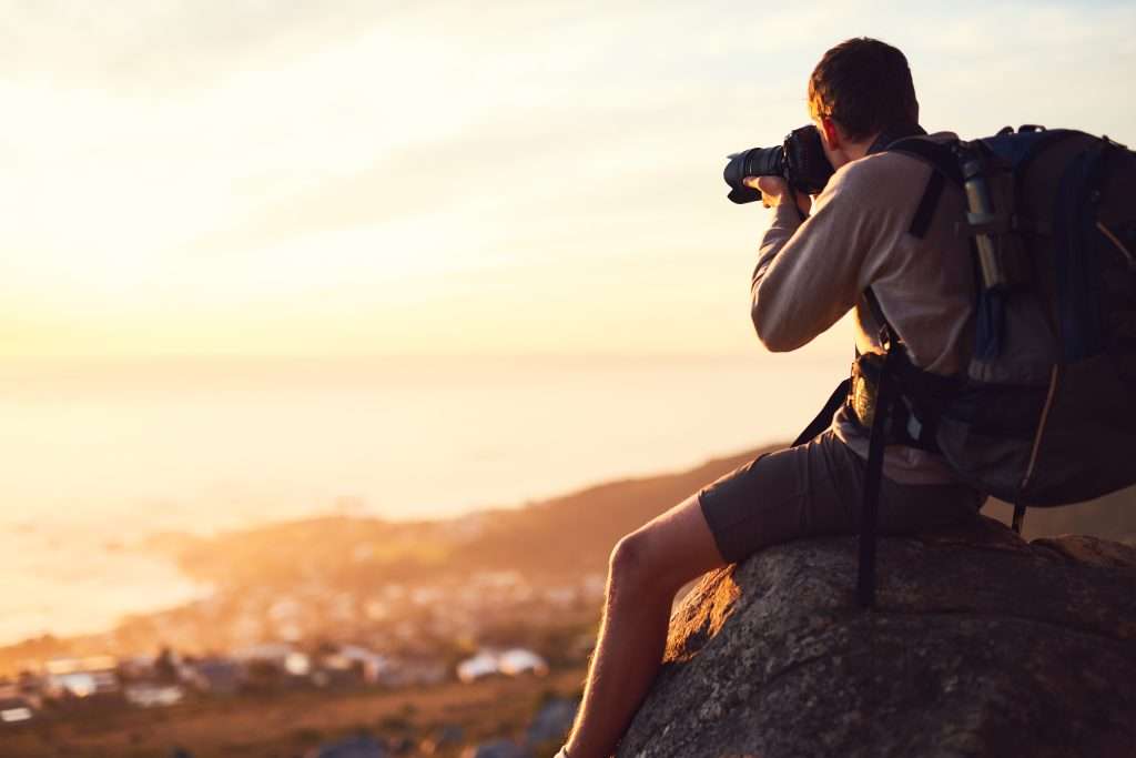 A man with a backpack is taking a picture of the ocean.