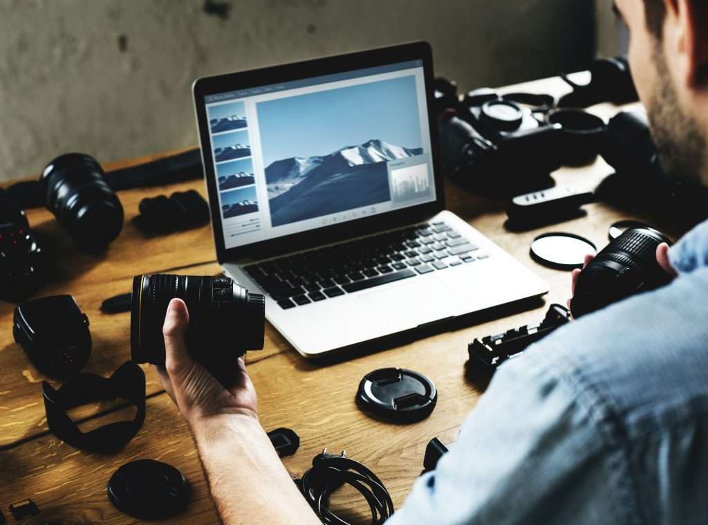 A man sitting at a desk with a laptop and camera equipment.